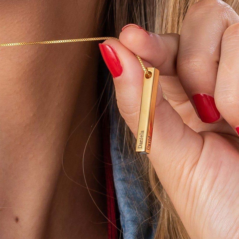 May include: Gold bar necklace with the names "Daniela" and "David" engraved on it.