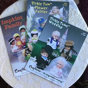 May include: Three knitting pattern books for dolls. The covers feature illustrations of dolls dressed in various outfits. The titles are "Impkins Family", "Tickle Tum Flower Fairies", and "Tickle Tums Wedding".