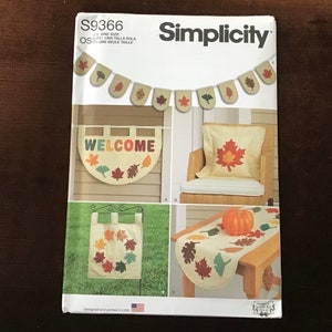 May include: Simplicity sewing pattern S9366 for autumn-themed home decor. The pattern includes instructions for making a welcome banner, a cushion, a table runner, and a wreath. The pattern is designed and printed in the USA.