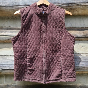 May include: A quilted brown vest with a zipper closure. The vest has a stand-up collar and sleeveless design.