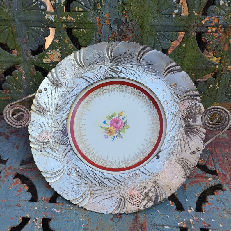 May include: A silver serving dish with a raised floral design and a red and white center plate with a floral design. The dish has a handle on each side.