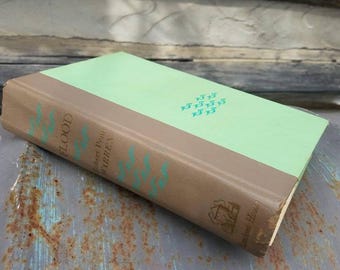 May include: A vintage hardback book titled "The Flood" by Robert Penn Warren. The book has a brown cover with a green spine and a green and brown dust jacket. The book is on a rusty metal surface.