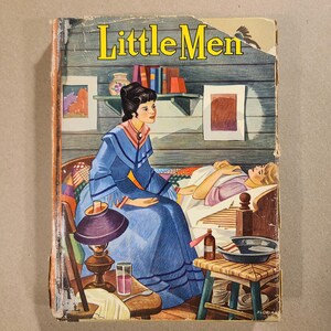 May include: Vintage book cover titled "Little Men." The illustration depicts a woman in a blue dress seated near a bed where a person is resting. A lamp, a glass, and a small table with a bowl and bottle are in the foreground. The background shows a shelf with books and artwork.