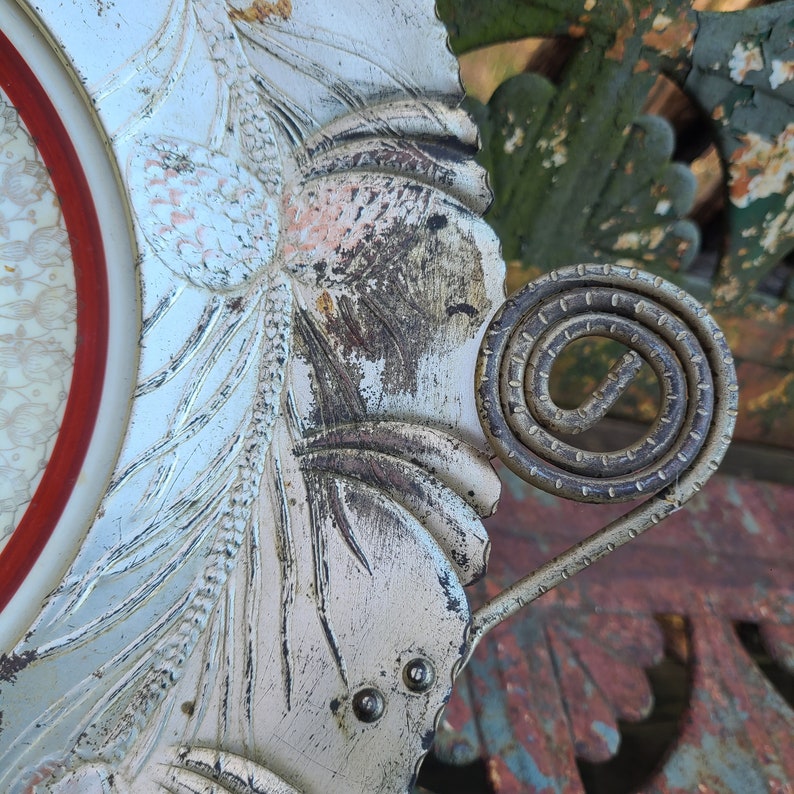 May include: A white metal tray with a decorative floral design and a spiral metal handle. The tray has a worn, aged look with some rust and discoloration.