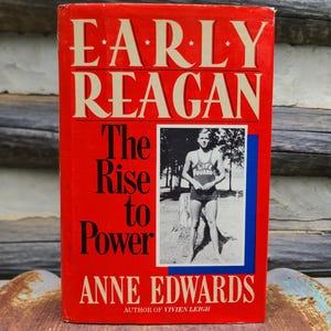 May include: A hardcover book titled "EARLY REAGAN The Rise to Power" by Anne Edwards. The cover is red with white lettering and a black and white photo of a man in a lifeguard uniform. The book is on a wooden surface.