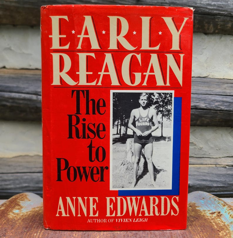 May include: A hardcover book titled "EARLY REAGAN The Rise to Power" by Anne Edwards. The cover is red with white lettering and a black and white photo of a man in a lifeguard uniform. The book is on a wooden surface.