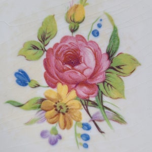 May include: A vintage floral design featuring a pink rose, yellow flower, and blue and purple accents on a white background.