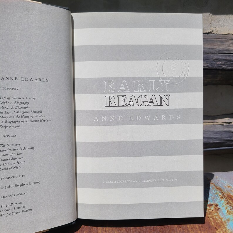 May include: An open book with the title "Early Reagan" by Anne Edwards. The book cover has a gray and white striped pattern. The left page lists other books by the author.