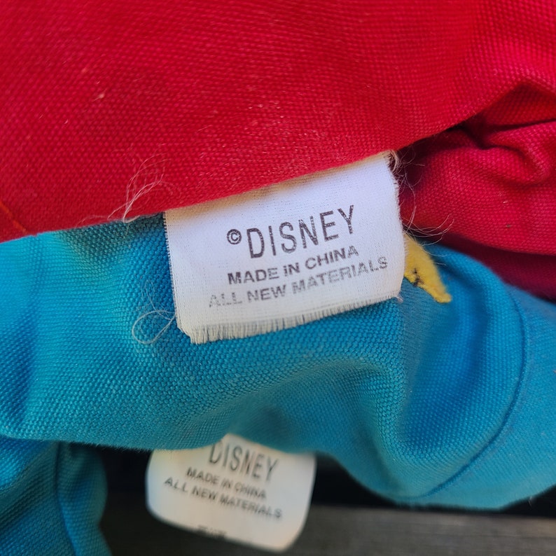 May include: Close-up of two white fabric labels sewn onto a blue and red fabric. The labels read "&copy; DISNEY MADE IN CHINA ALL NEW MATERIALS".