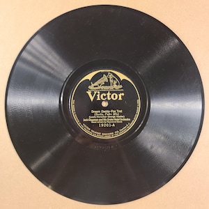 May include: A black circular vinyl phonograph record with a central gold and black label. The label features the Victor brand logo, the text Dream Daddy-Fox Trot, and credits Jack Chapman and His Drake Hotel Orchestra with vocal refrain by Raymond Davis.