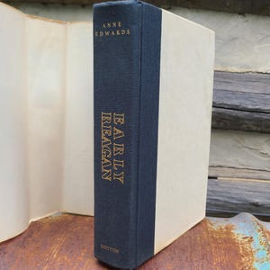 May include: A hardcover book titled "Early Reagan" by Anne Edwards. The book has a navy blue spine with gold lettering and a cream-colored cover. The book is displayed on a rustic wooden surface.