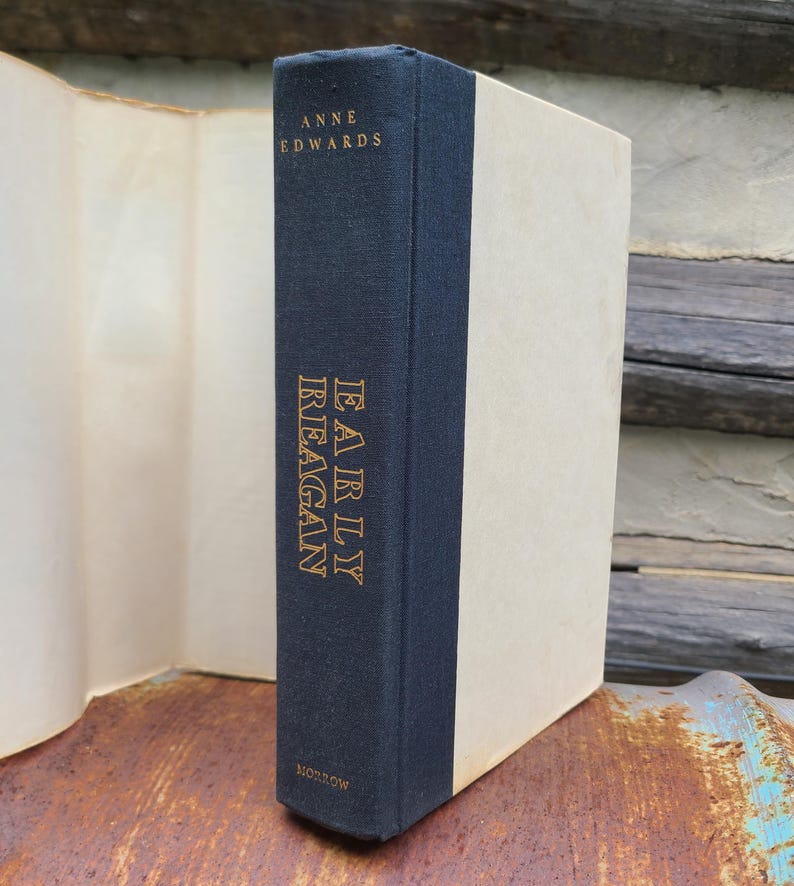 May include: A hardcover book titled "Early Reagan" by Anne Edwards. The book has a navy blue spine with gold lettering and a cream-colored cover. The book is displayed on a rustic wooden surface.