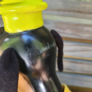 May include: Close-up of a black and yellow cartoon dog figurine. The dog has a yellow hat and black ears. The figurine is made of plastic and has a glossy finish.