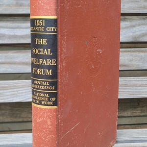 Peut inclure: Un livre vintage intitulé "The Social Welfare Forum" de 1951, publié par Columbia University Press. Le livre a une couverture brun-rougeâtre usée avec des lettres noires sur le dos, dont "Atlantic City" et "National Conference of Social Work."