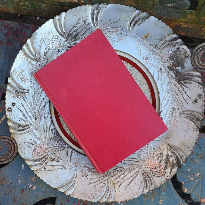 May include: A red hardcover book with a decorative design on the cover, resting on a silver tray with a floral pattern.