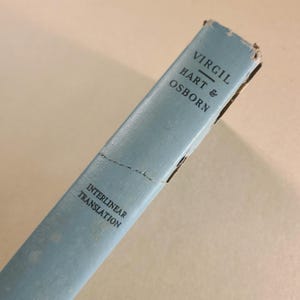 May include: A light blue book spine with the text "VIRGIL HART & OSBORN" printed vertically. Below, the text reads "INTERLINEAR TRANSLATION". The book shows signs of age and wear, with some damage to the edges.