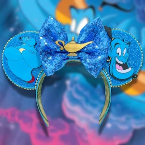 May include: Blue sequined bow headband with gold accents and character illustrations. Features a gold lamp charm and character illustrations of Genie and the Genie from Aladdin. The headband is a fun accessory.