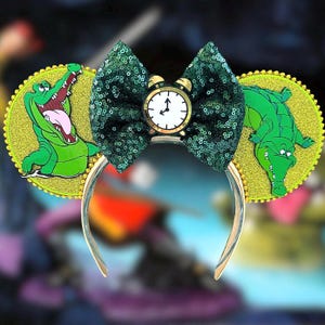 May include: Green and gold Mickey Mouse ears with a green bow and a clock face in the center. The ears feature a green alligator with a toothy grin on one side and a green alligator with its mouth closed on the other side.