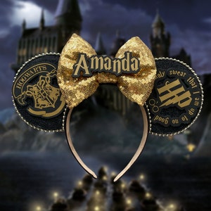 May include: Black and gold Minnie Mouse ears with a gold glitter bow and a black and gold Hogwarts crest on one ear and the text "Amanda" on the other ear. The ears are in front of a blurry image of Hogwarts castle.