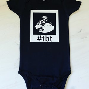 Op de afbeelding: Zwarte baby romper met een witte echografie afbeelding en de tekst "#tbt" gedrukt op de voorkant.