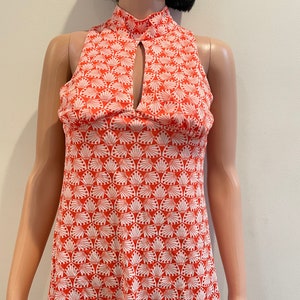 May include: A sleeveless, red and white patterned top with a high neckline and a keyhole opening at the front. The pattern features white stylised fans on a red background.