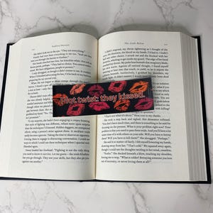 Peut inclure: Marque-page noir avec l'inscription "Plot twist: they kissed" et des empreintes de baisers rouges et oranges. Il est placé dans un livre ouvert, entre les pages, pour marquer la page.
