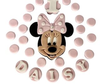 May include: Pink and white fondant decorations for a cake, featuring a Minnie Mouse head, the number 1, and the name "Daisy".