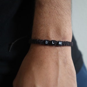 May include: A brown braided bracelet with black beads that spell out "BLM".