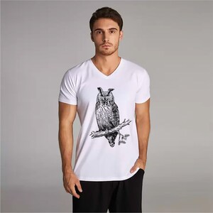 May include: White V-neck t-shirt with a detailed black and white illustration of an owl on a branch. This graphic tee is a classic design, suitable for casual wear. The shirt is made of a soft, comfortable material.