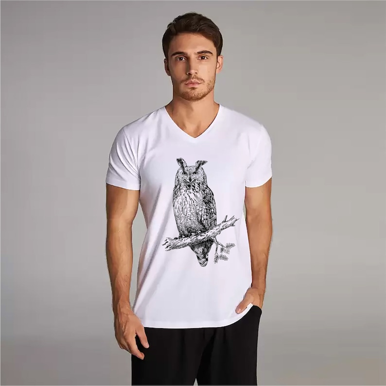 May include: White V-neck t-shirt with a detailed black and white illustration of an owl on a branch. This graphic tee is a classic design, suitable for casual wear. The shirt is made of a soft, comfortable material.