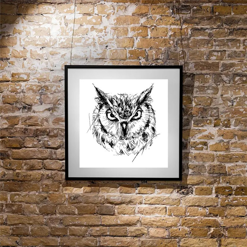 May include: A framed black and white sketch of an owl's face. The artwork is displayed on a white background within a black frame, hanging against a textured brick wall. The owl's detailed features are emphasized.