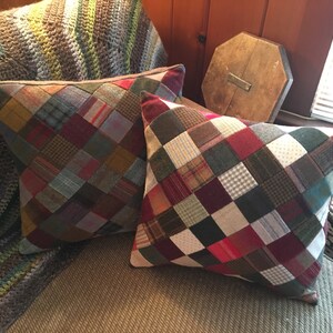 May include: Two square patchwork pillows with a diamond pattern. The pillows are made of various shades of brown, red, green, and white fabrics. The pillows are sitting on a couch.