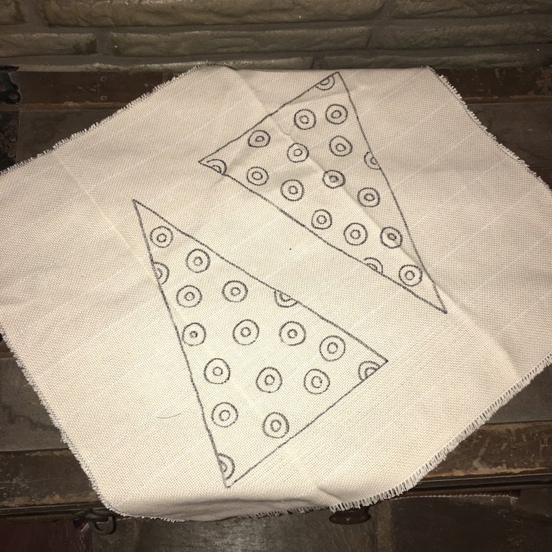 May include: A white fabric with two triangles drawn on it. The triangles are filled with a pattern of black circles.