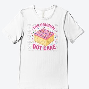 May include: A white short-sleeve t-shirt featuring a graphic of a square cake with pink frosting and colorful dots. The text above the cake reads THE ORIGINAL and the text below reads DOT CAKE. The background has a faint watermark pattern.