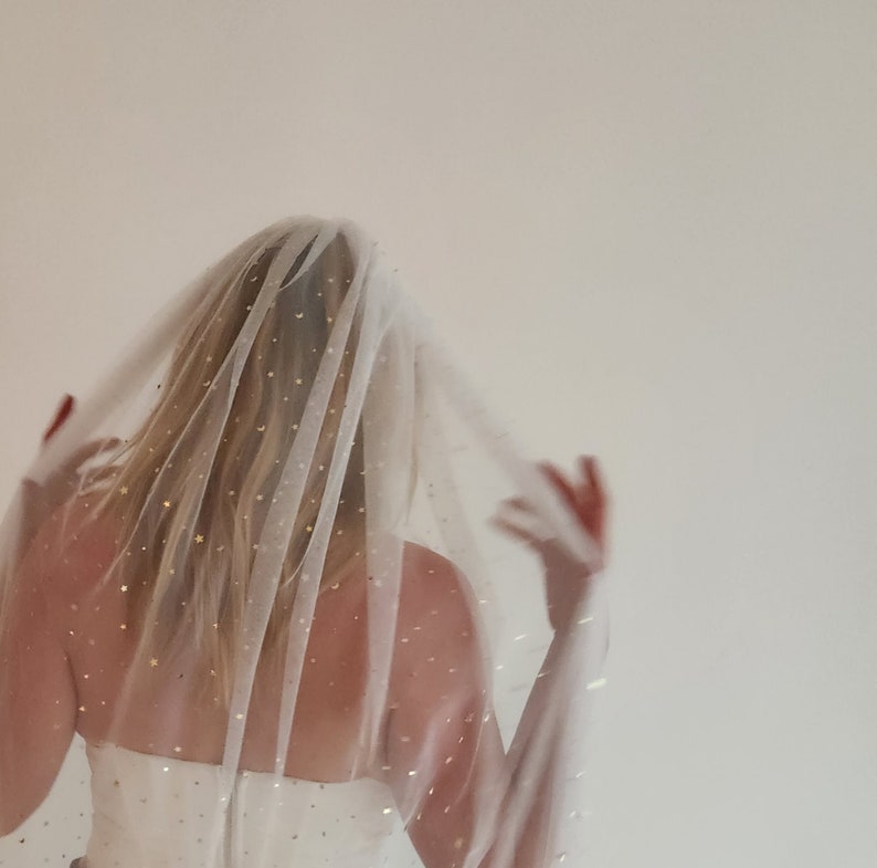Op de afbeelding: Een witte bruids sluier met gouden glittersterren die over de hele sluier zijn verspreid. De sluier is doorschijnend en delicaat, en de sterren voegen een vleugje glans toe.