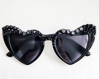 May include: Black heart-shaped sunglasses with rhinestones and the words "TIL DEATH" on the frames.
