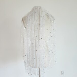 Op de afbeelding: Witte tule sluier met gouden sterretjes versiering. De sluier is gedrapeerd over een wit mannequin.