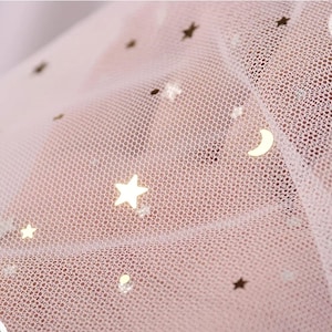 Op de afbeelding: Roze tule stof met gouden glittersterren en een halve maan.