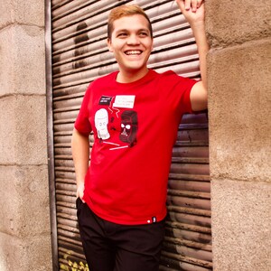 May include: A red short-sleeved t-shirt featuring a graphic print of two characters in speech bubbles with the text "JOIN THE DARK SIDE" and "NO, I AM YOUR FATHER". The shirt has a small black and white logo tag on the bottom hem.