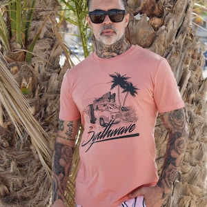 May include: A man wearing a peach colored t-shirt with a graphic of a vintage van, palm trees, and the text "Synthwave". He is also wearing pink and white striped shorts.
