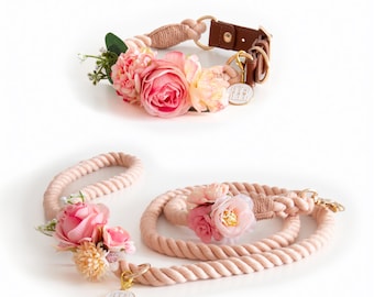 May include: A dog collar and leash set in a light pink rope design. The collar features a brown leather buckle and is adorned with pink and peach-colored flowers. The leash has a matching floral arrangement and gold-colored hardware.