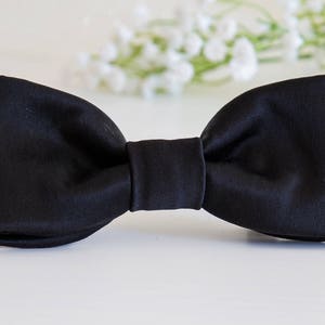 May include: A black bow tie made of satin fabric.