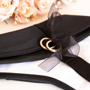 Puede incluir: Collar de tela negro con una cinta negra y dos anillos dorados. El collar est&aacute; unido a una correa negra.