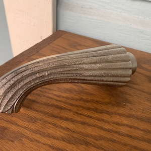 May include: A silver-toned, decorative, curved handle with a textured, ribbed design.