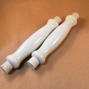 May include: Two white ceramic handles with a rounded shape and a slightly textured surface.