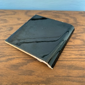 May include: A black ceramic tile with a rounded edge. The tile has a glossy finish.