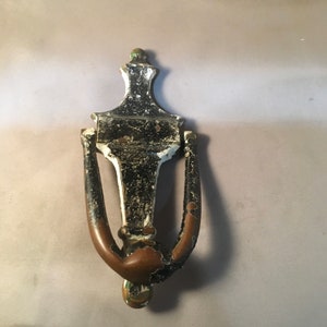 May include: A vintage black and brass door knocker with a decorative design. The knocker is in the shape of a bell with a ring handle.