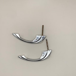 May include: Two silver cabinet door handles with a curved, modern design. The handles have a shiny finish and are attached to a metal screw.