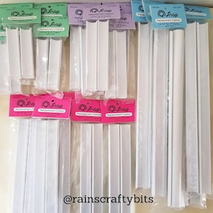 May include: A selection of white plastic Q-Snap replacement clamps for picture frames. The clamps are packaged in clear plastic bags with pink and green labels that say "Q-Snap Replacement Clamps" and list the size of the frame they are for. The sizes range from 8 1/2 inches to 14 1/2 inches.
