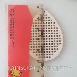 May include: A light-colored, teardrop-shaped wooden craft piece with evenly spaced holes, next to a ruler. The ruler shows measurements in inches. The text "RAINSCRAFTYBITS@ETSY" is visible at the bottom.